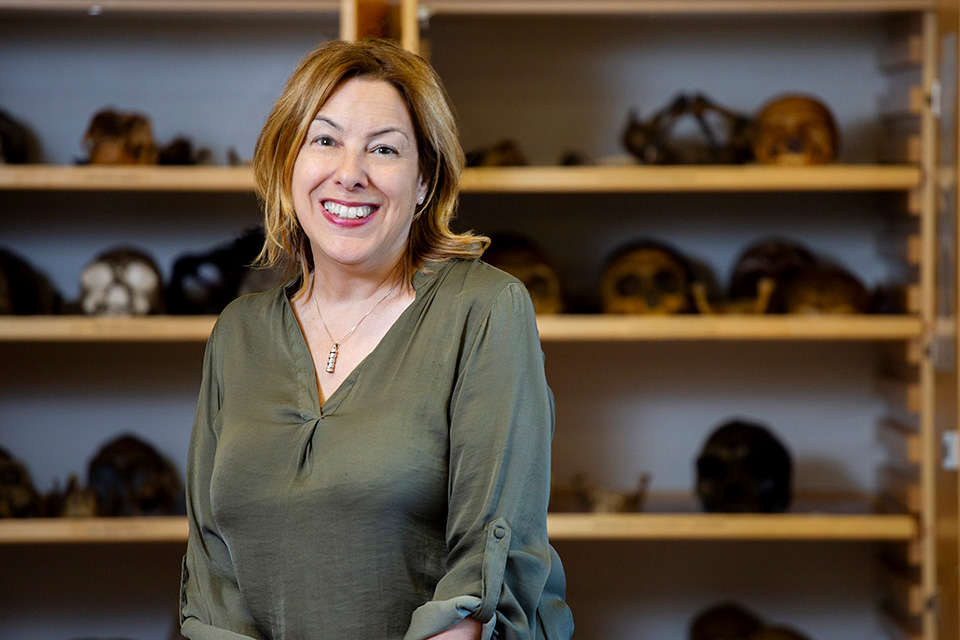 University of Victoria paleoanthropologist April Nowell sits in a lab with bones seen behind her.
