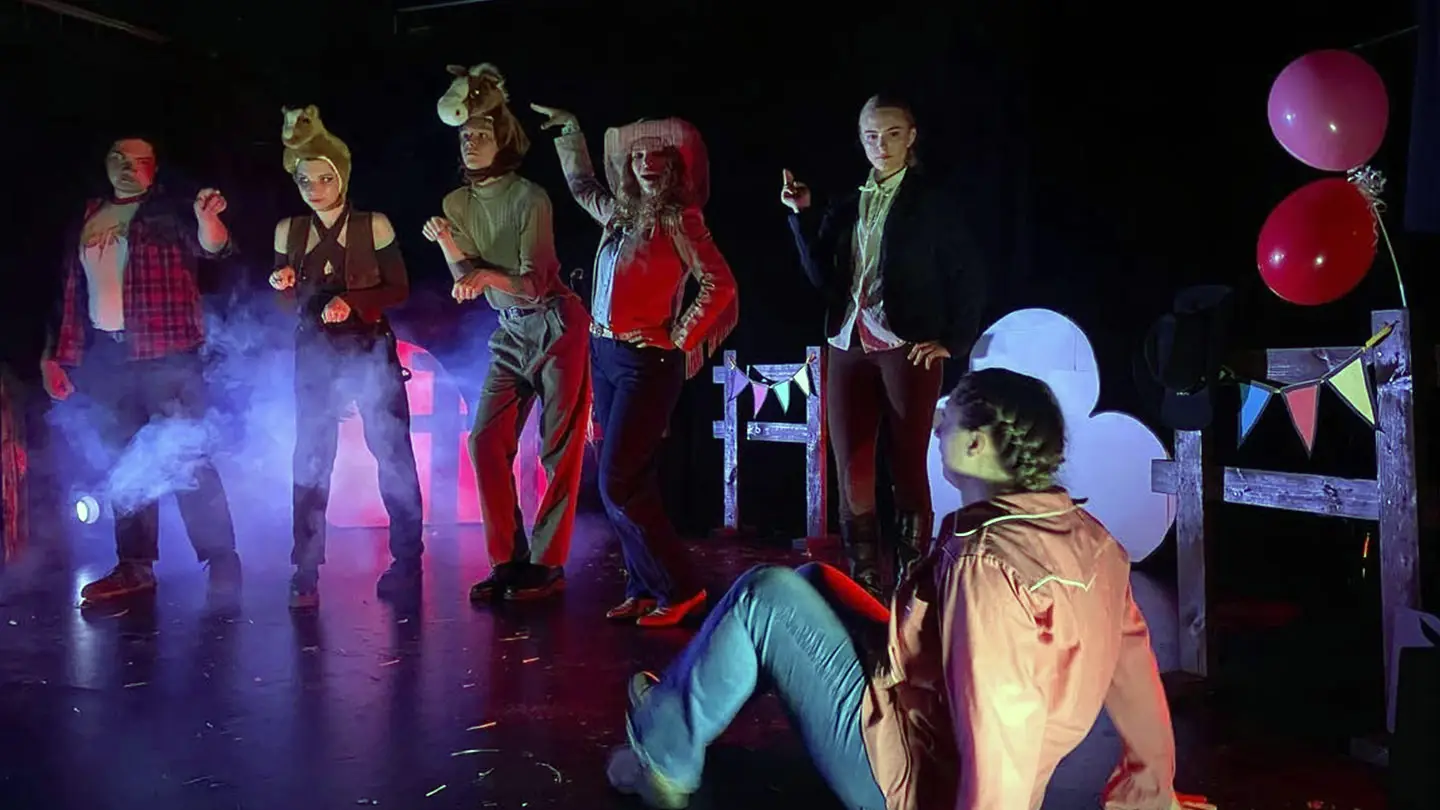 A group of actors in a scene on a backlit theatre stage.