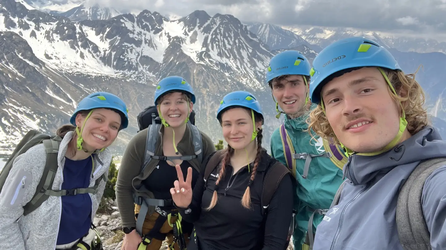 A group of people wearing blue helmets take a group photo on a snowy mountain.
