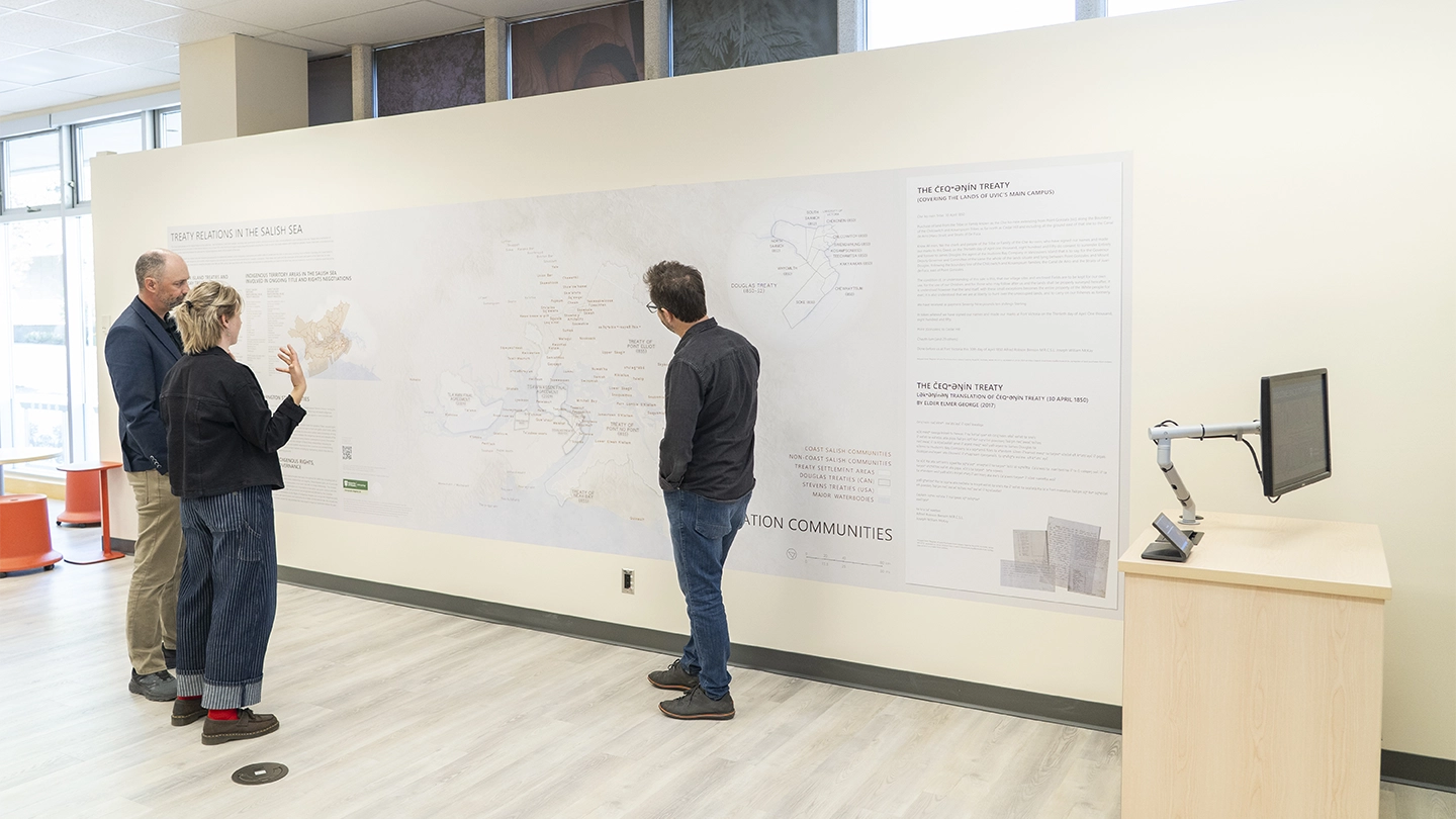 Three people standing in front of a wall length map.