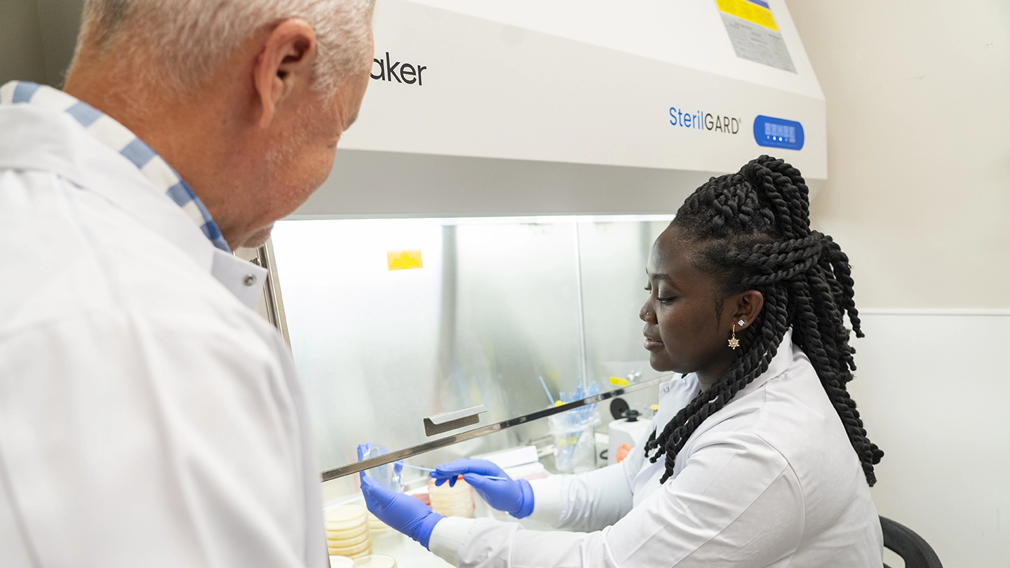 Two people look at a petri dish in a lab.