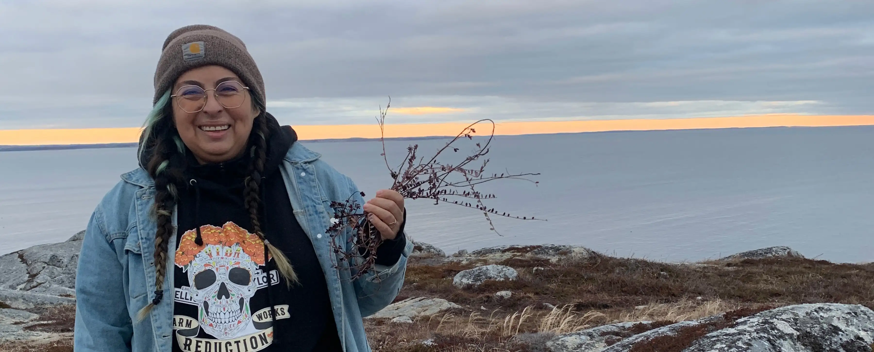 A student holds up a bundle of plants on a rocky beach.