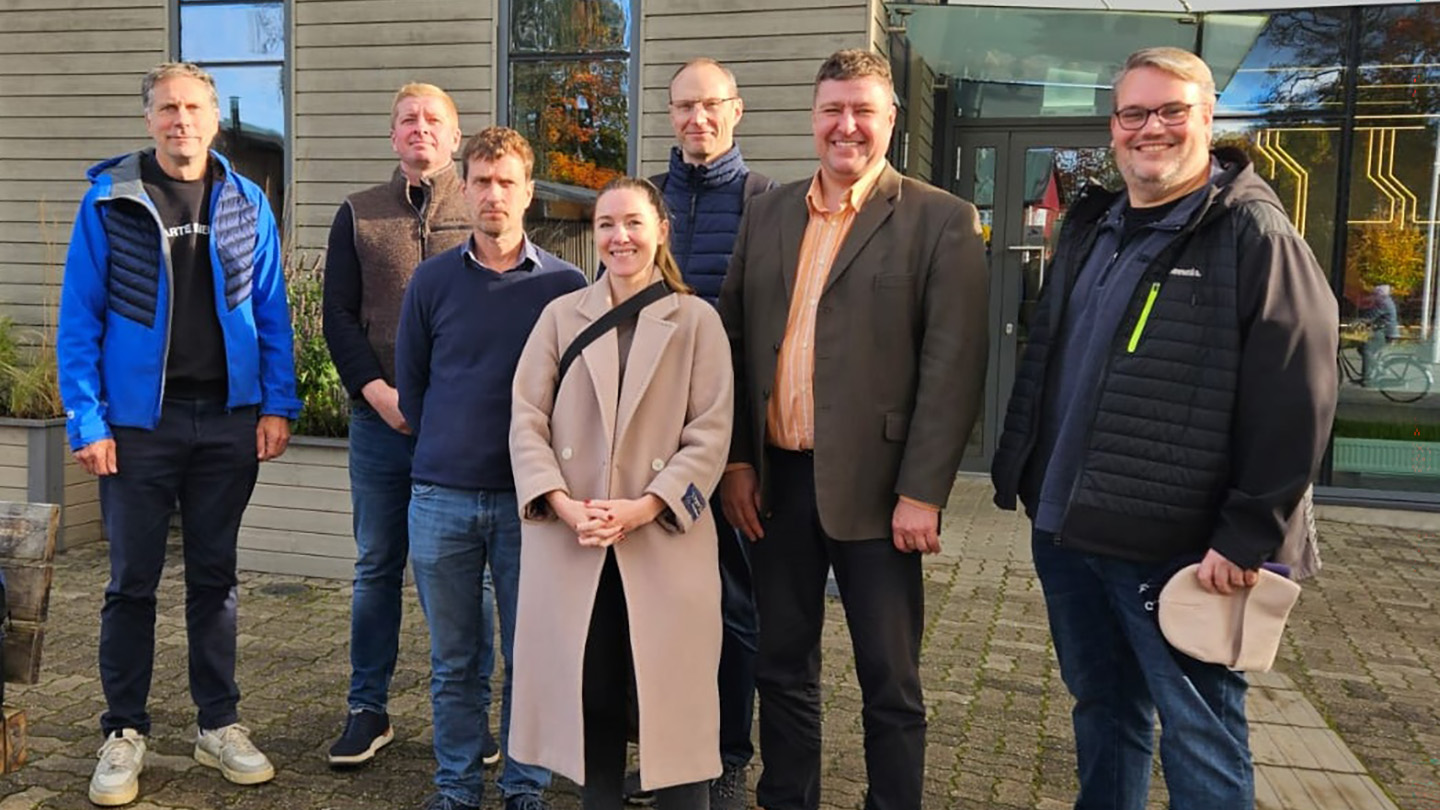 A group of seven representatives from ACET and EISEA standing outdoors in front of a modern building on a sunny day, wearing casual and business-casual clothing, posing together during the initial meeting for this partnership.