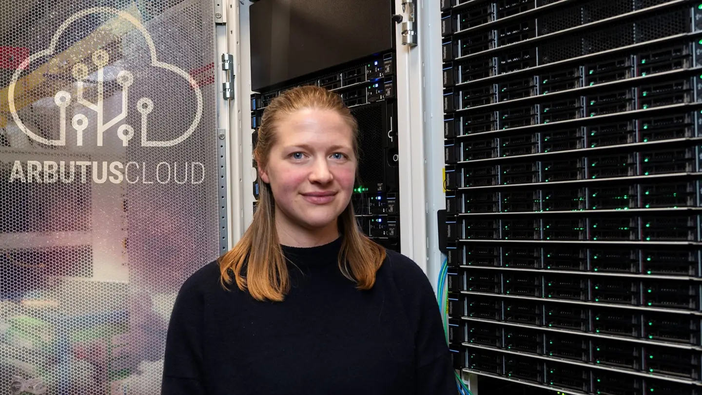 Sarah Huber stands beside a sign for Arbutus Cloud, the high-performance cloud computing centre housed at UVic.