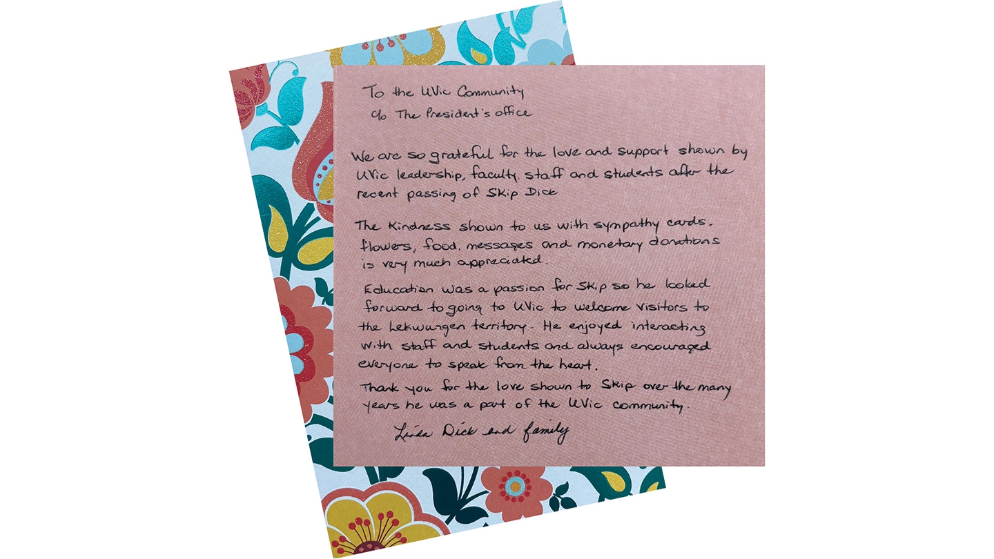 A handwritten note on light pink paper addressed to the UVic community, expressing gratitude for the kindness and support shown to the family after the passing of Skip Dick. The letter is signed by Linda Dick and family. A colourful flower print is behind the pink paper.