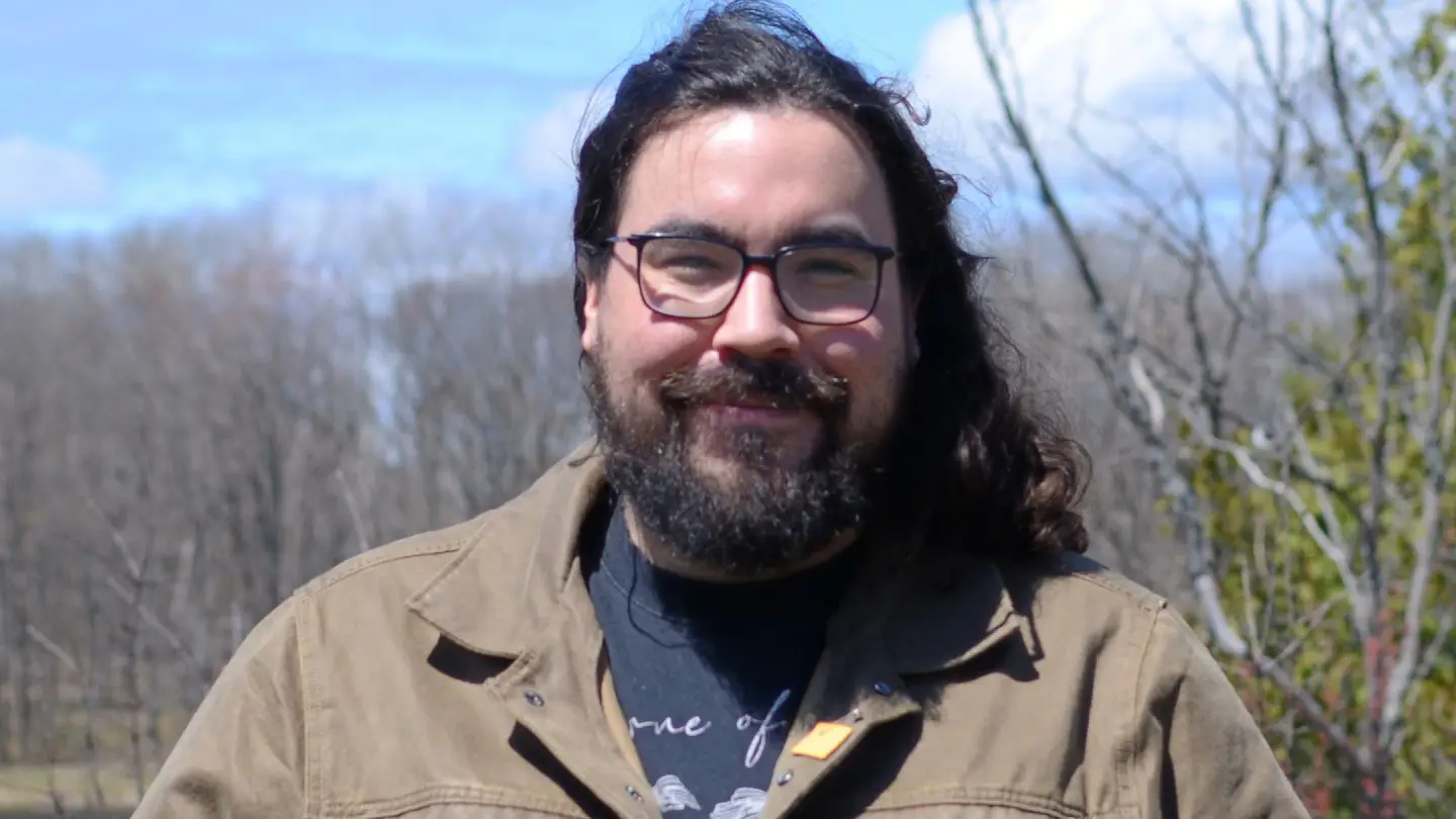 Mathew is standing in a forested area and smiling.