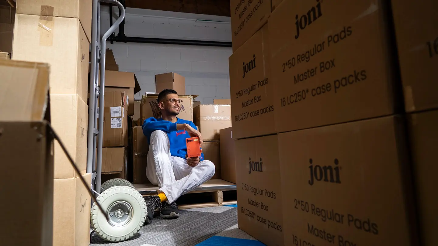 Jayesh Vekariya sits amongst shipping boxes and holds a "joni" box.