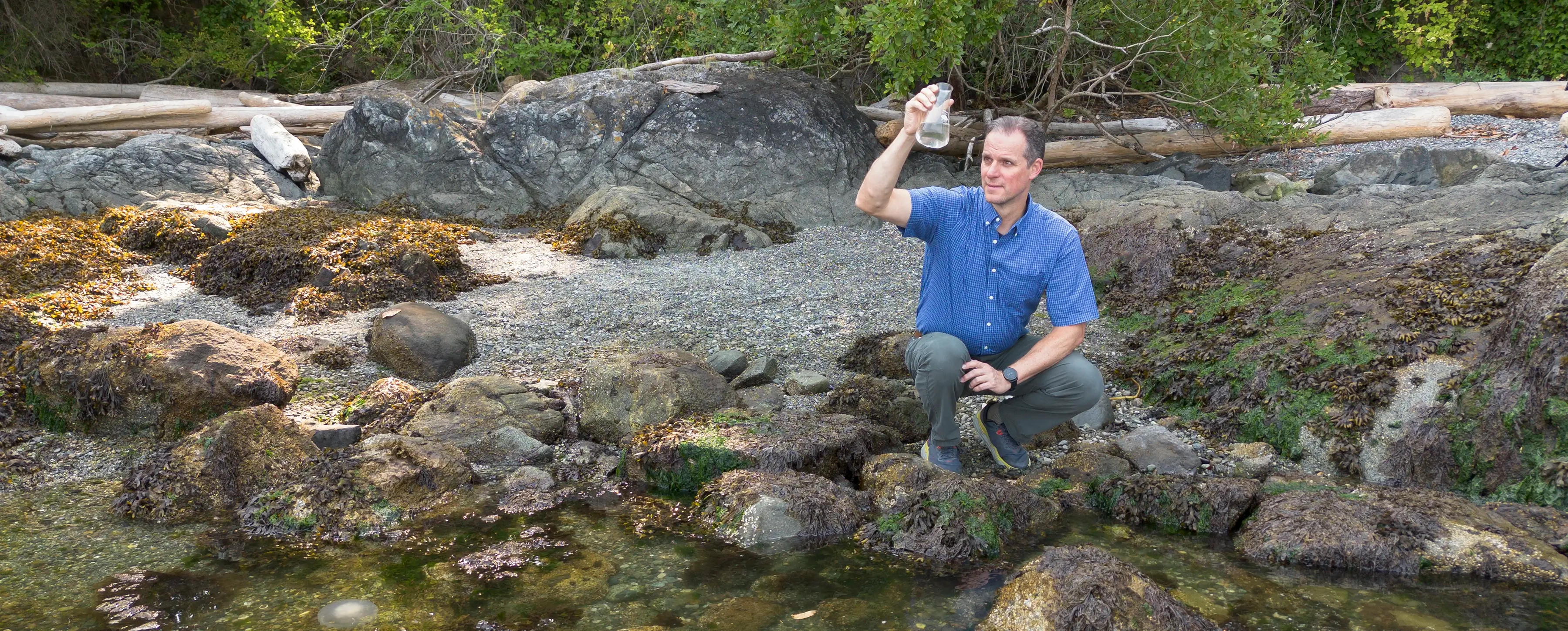 Adrian Marchetti kneeling by the ocean, holding up a flask full of ocean water.